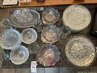 Overview photo of various clear glass bowls, plates, and platters with textured and patterned surfaces, showing grape motifs and pointed edges.