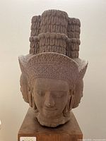 Front view of the four-faced stone head sculpture on wood base