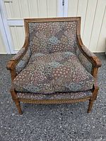 Front view of the French Louis XVI style armchair showing floral fabric upholstery with carved wooden frame and brass nailhead trim.