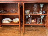 Wide view of cabinets containing glass bowls, ceramic bowls and dishes, glass vases, candle holders, and small oil lamp