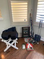 Photo shows white folding stool, golf magazines, shadow box with golf balls, two umbrellas, golf clubs, and other golf items on floor near window.