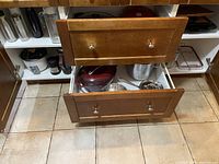 Wood cabinet with open drawers and doors showing red Dutch ovens, metal cookware, pots, and utensils inside cabinetry.