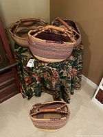 Four handcrafted large African woven baskets arranged on and around a round table with floral tablecloth.