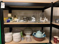 Full shelves showing various home decor and kitchenware items including candles, candle holders, ceramic bowls, glassware, scarves, kitchen scissors, teapot and more.