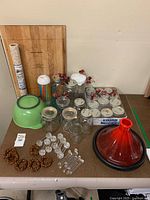Overview of all kitchen items on a brown surface including pastry board, jars, plastic straws, mixing bowl, napkin rings, glass stirrers, and tagine pot.