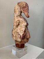 Side angle view showing detailed carving of bird figure on top and human face profile, mounted on acrylic base.