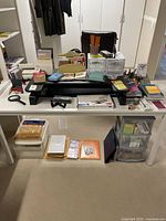Wide view of office supplies lot on and below a desk including books, notebooks, stationery, plastic drawer organizers, pencils, and other office accessories