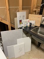 Lot contents arranged near utility sink with canvases stacked and paint sets and paint tube on counter.