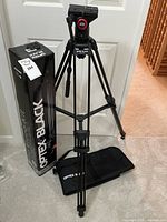 Full view of Optex Black OBVK50 tripod fully extended with original box and black carrying case on floor