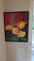 Front view of the signed fruit still life painting showing citrus fruits and grapes with black frame.