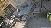 Glass-top dining table surrounded by metal frame chairs with mesh seats and backs, tan color.
