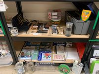Wide view of two shelves showing various painting and art supplies including crayons, watercolor sets, instructional book, toolbox, and other containers.