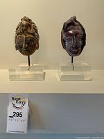 Front view of the pair of carved stone face masks on stands showing the colors and size.