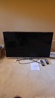 Samsung 46 inch LED TV on beige carpet with power cord, two remote controls, and printed user manual in front.