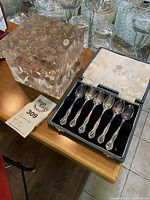 Set of six Mappin & Webb silver plated demitasse spoons displayed in blue velvet lined case next to a resin cube filled with Canadian pennies.