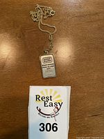 Silver bar pendant laid out on wooden surface with auction bidding card numbered 306 below it.