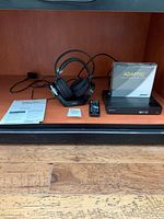Sony wireless headphones on charging dock, Bose ADAPTiQ system box, remote, cables, and manuals on shelf