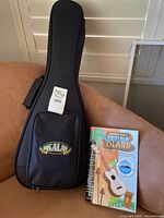 Kala black padded ukulele case standing upright beside songbook on sofa