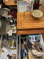 Photo showing large wooden cutting boards, salt and pepper grinders, a decorative plate, and various kitchen tools in drawers including utensils and other small tools.