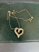 Gold-tone chain necklace with a heart shape pendant lying flat on black textured surface.
