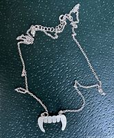 Photo showing full necklace with pendant resembling fangs on textured black background