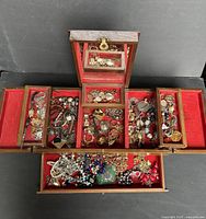 Top-down view of the wooden jewelry box with multiple compartments filled with assorted costume jewelry and watches on a red velvet lining.