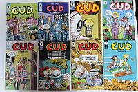 Photo showing the full set of 8 CUD comic book issues laid out in two rows of four featuring colorful illustrated covers with various characters and scenes.