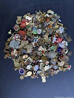 Photo showing large pile of assorted vintage pins of various colors and shapes, spread in a circular pattern on a dark background.