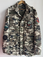 Full front view of men's Guess camouflage jacket hanging on wooden hanger, showing patches on front and sleeves.