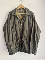 Full front view of olive green insulated men's North Face over shirt hanging on wooden hanger, showing button-up front and collar.
