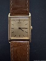 Front close-up view of square gold-tone Seiko watch face with minimal gold hour markers and hands.