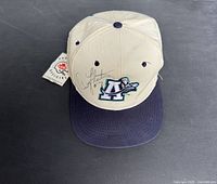 Front angled view showing beige cap with navy brim, Argos logo, Doug Flutie signature, and attached original tag.
