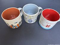Photo of three Starbucks city mugs showing varying interior colors and exterior city-themed designs.