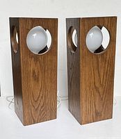 Pair of vintage lamps standing upright with dark stained wooden cube frames with circular cutouts and white spherical bulbs inside, placed side by side with long visible cords.
