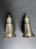 Pair of vintage sterling silver salt and pepper shakers on black surface showing shape and size.