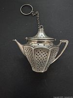 Full view of the perforated silver tea diffuser shaped like a teapot with a keyring attached.