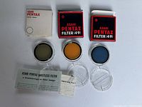 Three circular colored filters (green, orange, blue) alongside their original boxes and plastic cases, and an informational leaflet about Ghostless filter technology.