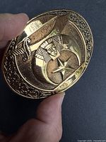 Close-up photo showing the detailed front of the gold plated Shriners belt buckle held in hand for size reference.