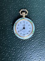 Top view of vintage small ladies Swiss Made pocket watch dial showing white face with black stylized Arabic numerals and black hands, gold-tone winding crown and ornate bow.