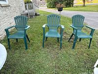 Three green plastic Adirondack style patio chairs placed outdoors on grass, showing overall state and design.