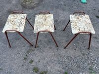Front view of three vintage stools aligned side by side, showing their marble-patterned seats and metal tubular frames with visible rust color.