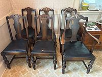 Six matching wooden dining chairs with dark carved backs, black upholstered seats, one with arms (captain chair), others armless.