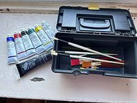 Set of nine paintbrushes in a black plastic carry case, paintbrushes show minimal wear, handles and bristles visible.