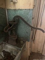 Oblique view of antique cast iron countertop water pump showing curved lever handle and spout mounted on green textured countertop.