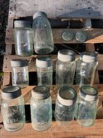 Full overhead view of eleven blue glass mason jars with blue metal lids arranged on wooden pallet, showing variable sizes and embossed branding.