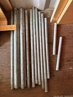 Fourteen galvanized steel pipes laid out on a wooden floor varying in length up to 36 inches, some with threaded ends.