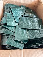Box containing many green zippered bags loosely stacked, showing quantity and packaging.