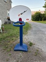 Front view of Little Tikes children's basketball hoop showing white backboard with logo, blue rim, and blue weighted base on grassy outdoor ground.