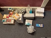 Photo showing several boxes and packages of Partylite candles and candle accessories arranged on the floor, including votive candles, tea lights, and glass candle holders.