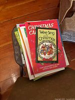 Top view of a small stack of piano and song books including 'Wee Sing for Christmas' and 'Christmas Carols' on a wooden surface.